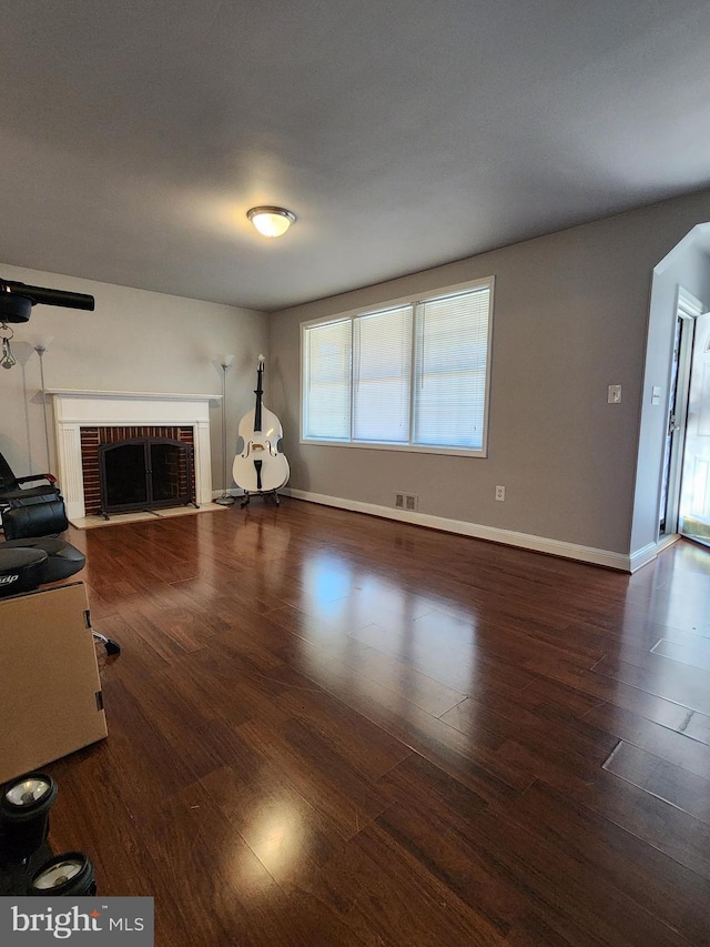 unfurnished living room featuring arched walkways, a fireplace, wood finished floors, visible vents, and baseboards