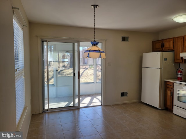 kitchen featuring brown cabinetry, white appliances, visible vents, and hanging light fixtures