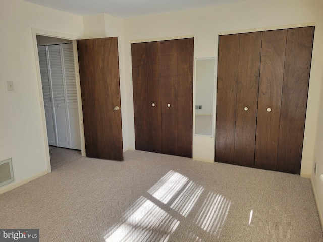 unfurnished bedroom featuring carpet floors, two closets, and visible vents