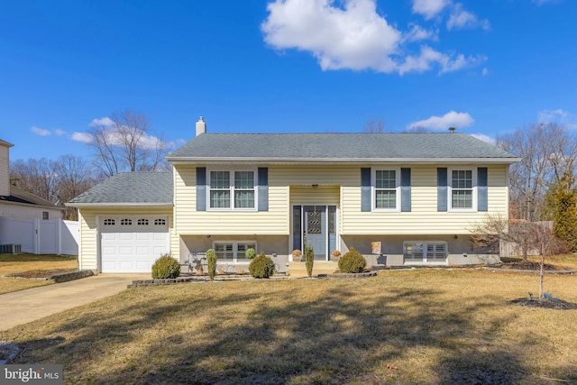 bi-level home with driveway, a garage, a chimney, fence, and a front lawn