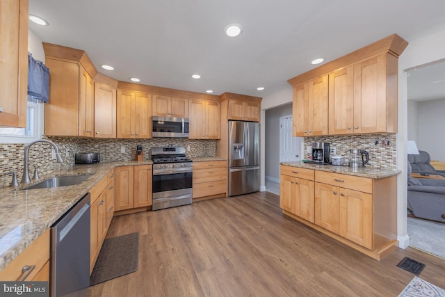 kitchen with stainless steel appliances, light brown cabinetry, a sink, and wood finished floors