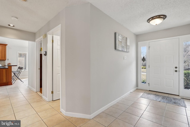 foyer featuring light tile patterned flooring, a textured ceiling, and baseboards