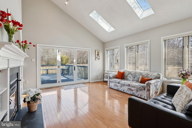 living room with baseboards, a fireplace with flush hearth, high vaulted ceiling, and light wood-style floors