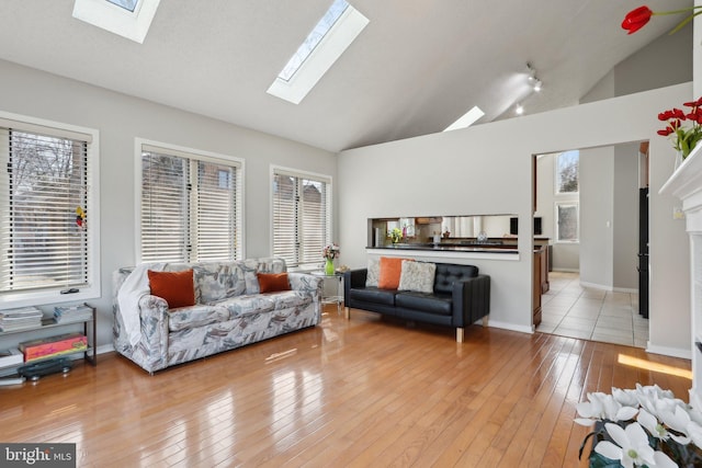 living area with baseboards, high vaulted ceiling, a skylight, and light wood finished floors