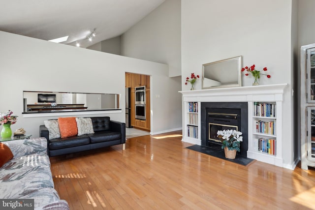 living room with a glass covered fireplace, wood finished floors, baseboards, and high vaulted ceiling