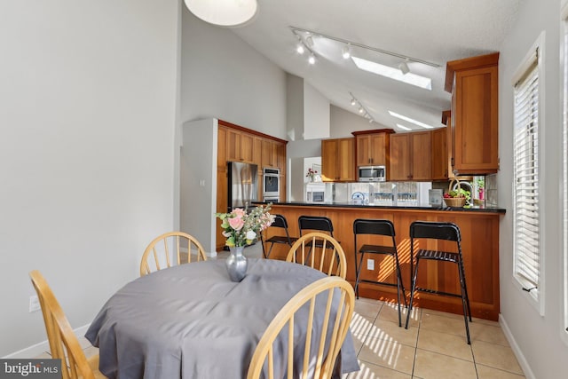 dining room with light tile patterned floors, a textured ceiling, baseboards, and vaulted ceiling