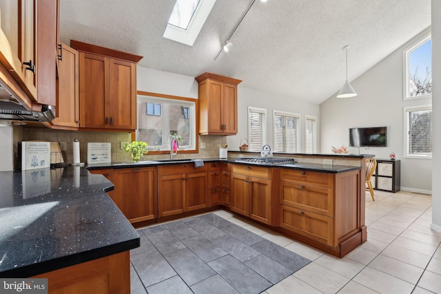 kitchen featuring lofted ceiling with skylight, brown cabinets, a peninsula, and a sink