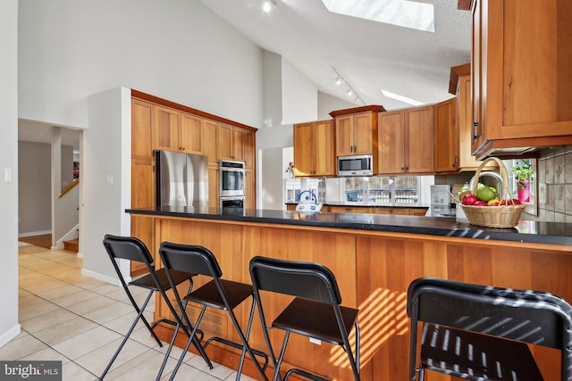 kitchen featuring brown cabinets, backsplash, appliances with stainless steel finishes, and light tile patterned flooring