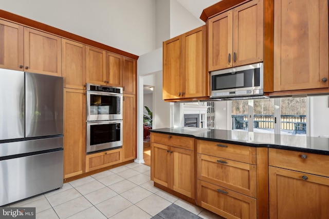 kitchen featuring brown cabinets, lofted ceiling, light tile patterned flooring, stainless steel appliances, and tasteful backsplash