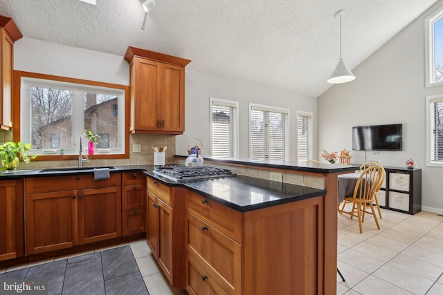 kitchen featuring lofted ceiling, light tile patterned floors, a peninsula, brown cabinetry, and a sink