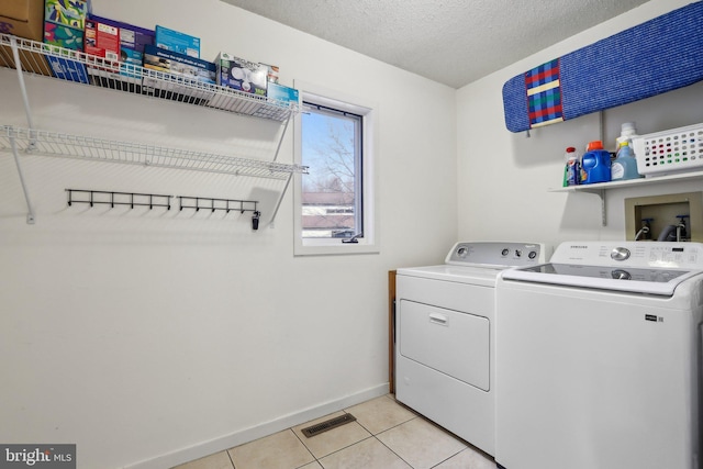 laundry room featuring visible vents, light tile patterned floors, laundry area, a textured ceiling, and separate washer and dryer