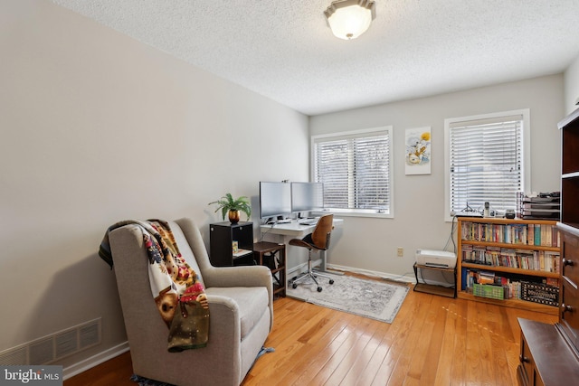 office area with hardwood / wood-style flooring, baseboards, visible vents, and a textured ceiling