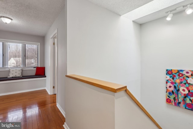 hall with track lighting, baseboards, hardwood / wood-style floors, an upstairs landing, and a textured ceiling