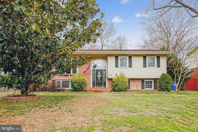 bi-level home with a front yard, a chimney, fence, and brick siding