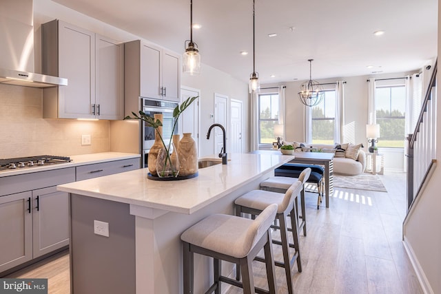 kitchen featuring light stone countertops, stainless steel appliances, gray cabinetry, wall chimney range hood, and a sink