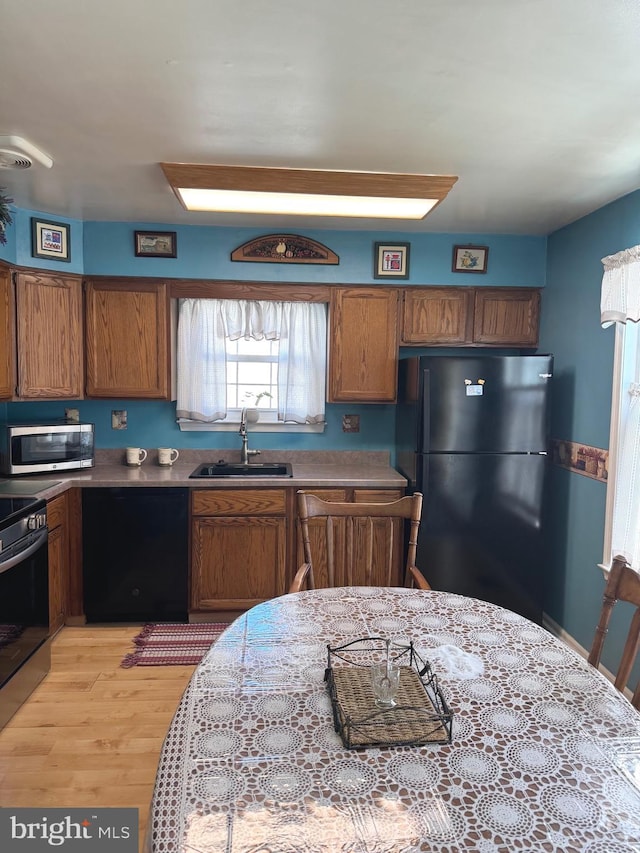 kitchen with brown cabinets, light countertops, light wood-style floors, a sink, and black appliances