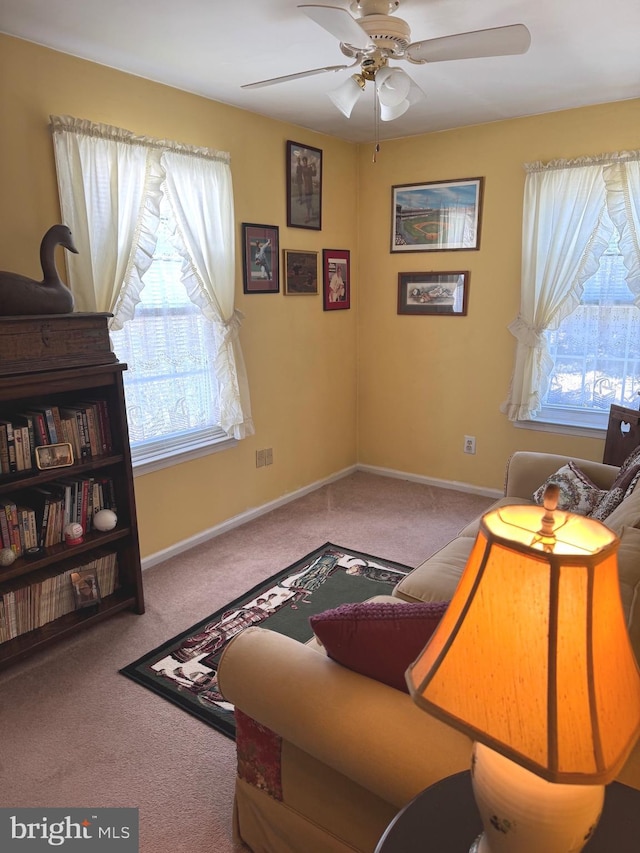 living area with ceiling fan, plenty of natural light, carpet flooring, and baseboards