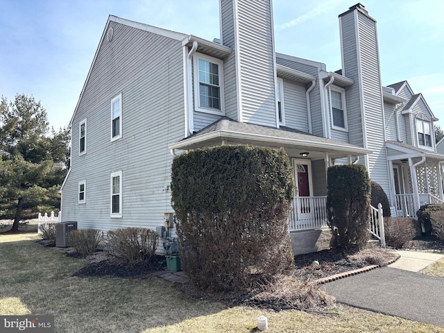 view of side of home featuring a yard, a porch, a chimney, and cooling unit