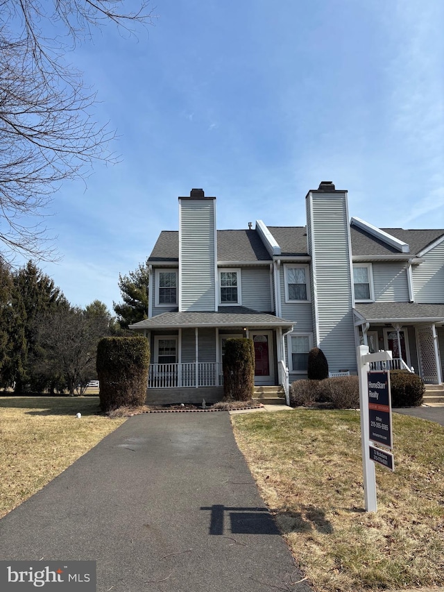 view of front of property with covered porch, a chimney, and a front lawn