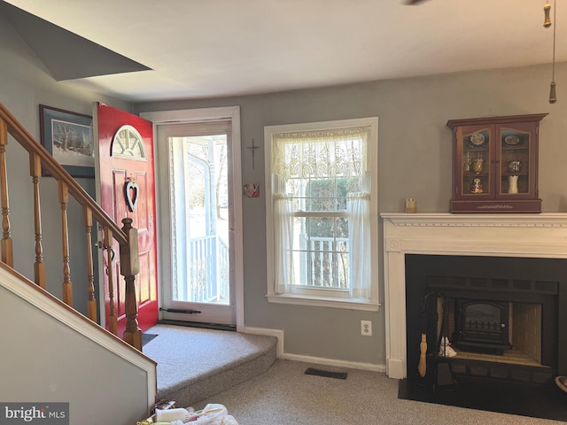 carpeted entryway featuring stairs, a fireplace with flush hearth, visible vents, and baseboards