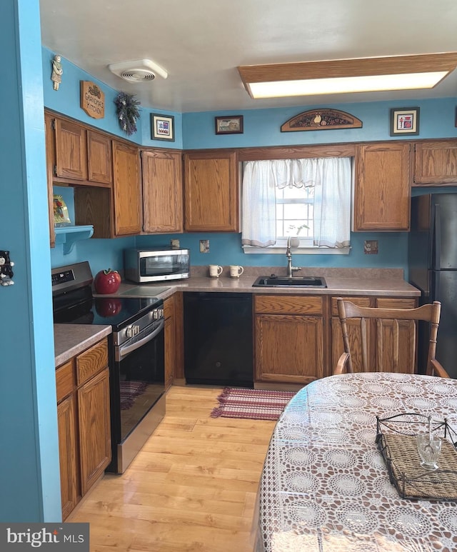 kitchen featuring light wood-type flooring, black appliances, brown cabinetry, and a sink