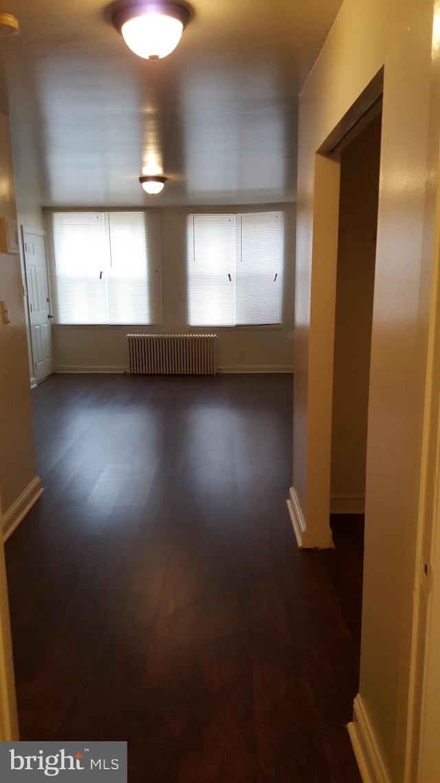 empty room featuring radiator, baseboards, and dark wood-style flooring