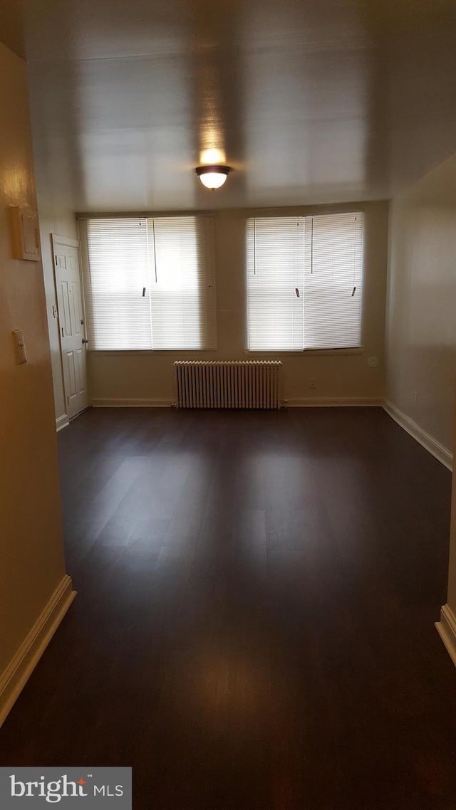 spare room with radiator heating unit, baseboards, and dark wood-type flooring