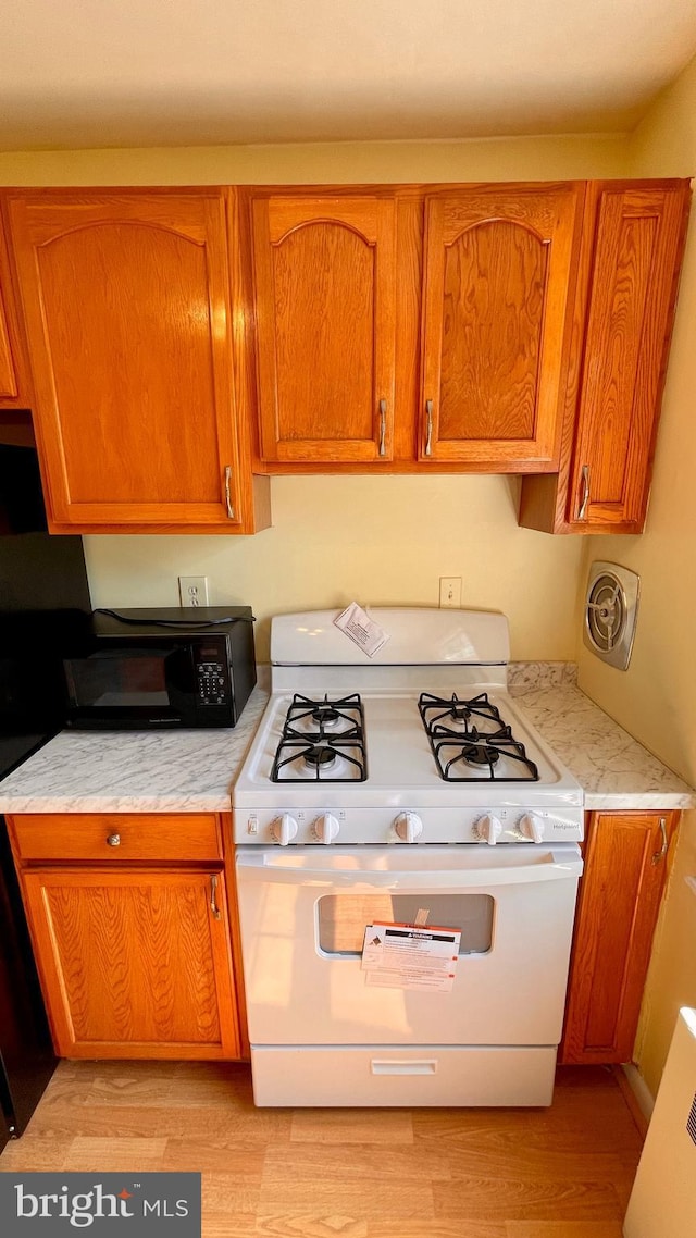 kitchen featuring black microwave, white gas stove, visible vents, light countertops, and brown cabinets