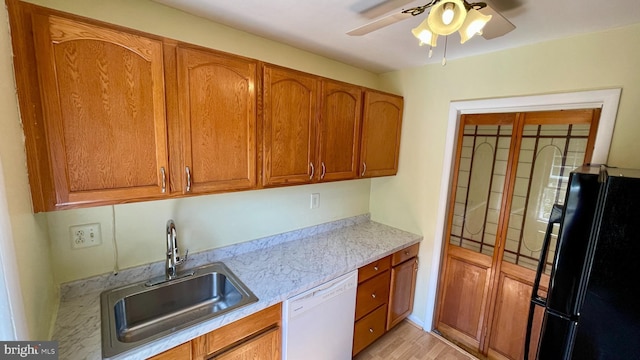 kitchen featuring brown cabinetry, freestanding refrigerator, white dishwasher, a sink, and ceiling fan