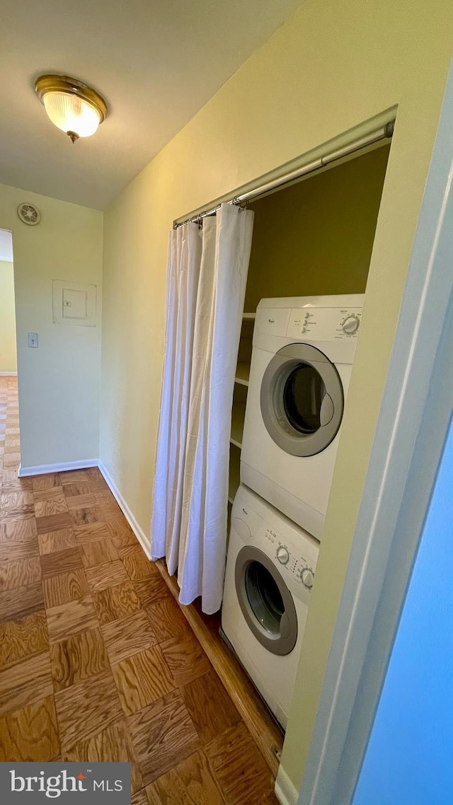 clothes washing area featuring laundry area, stacked washer / dryer, and baseboards