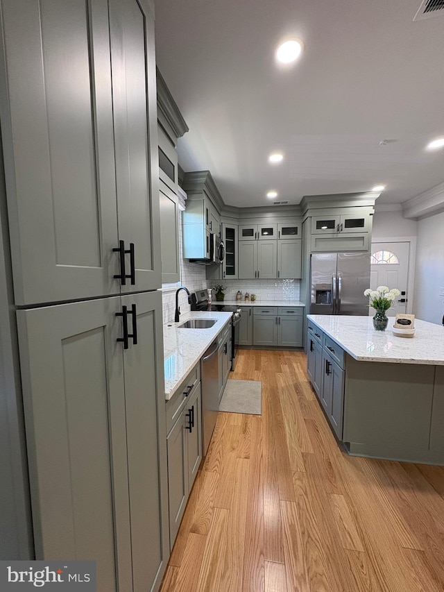 kitchen with gray cabinetry, a sink, appliances with stainless steel finishes, light wood-type flooring, and backsplash