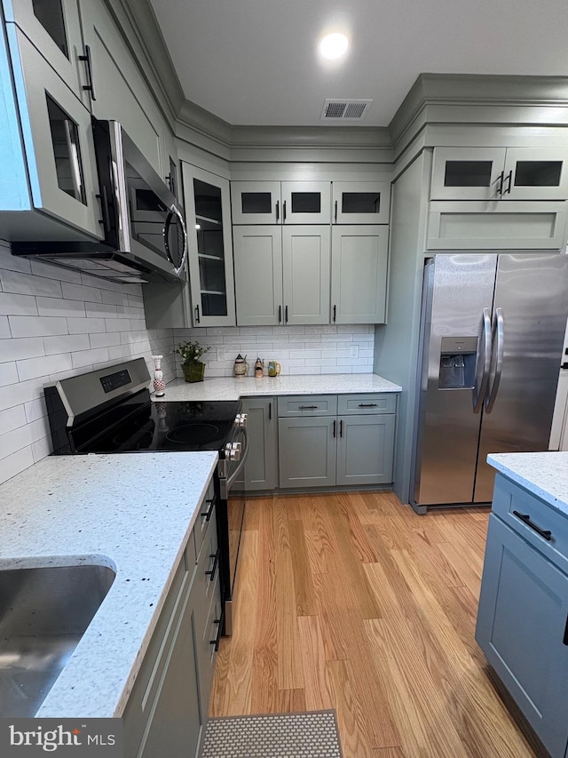 kitchen featuring visible vents, appliances with stainless steel finishes, gray cabinets, light wood finished floors, and tasteful backsplash