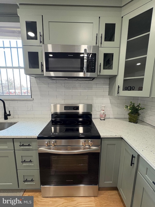 kitchen featuring gray cabinets, backsplash, appliances with stainless steel finishes, a sink, and light stone countertops