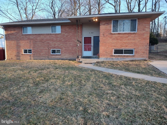 raised ranch featuring brick siding, fence, and a front lawn