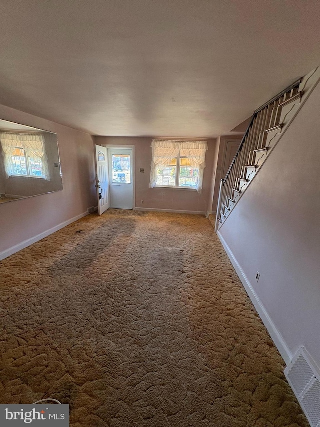 unfurnished living room featuring carpet floors, stairway, visible vents, and baseboards