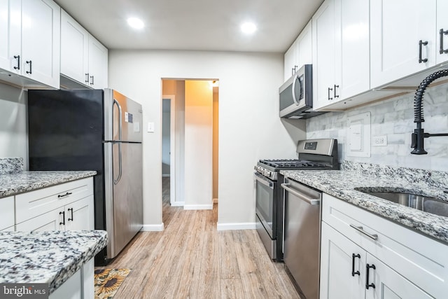 kitchen featuring light wood-type flooring, a sink, backsplash, appliances with stainless steel finishes, and white cabinets