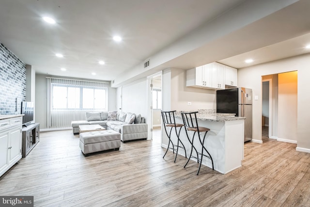 kitchen featuring a kitchen bar, light wood-style flooring, freestanding refrigerator, recessed lighting, and white cabinets