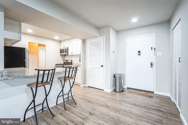 kitchen with stainless steel appliances, light wood-style floors, a breakfast bar, and white cabinets