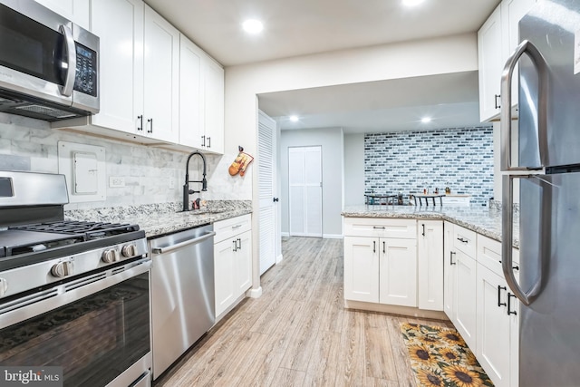 kitchen featuring appliances with stainless steel finishes, white cabinetry, light wood-style floors, and a sink