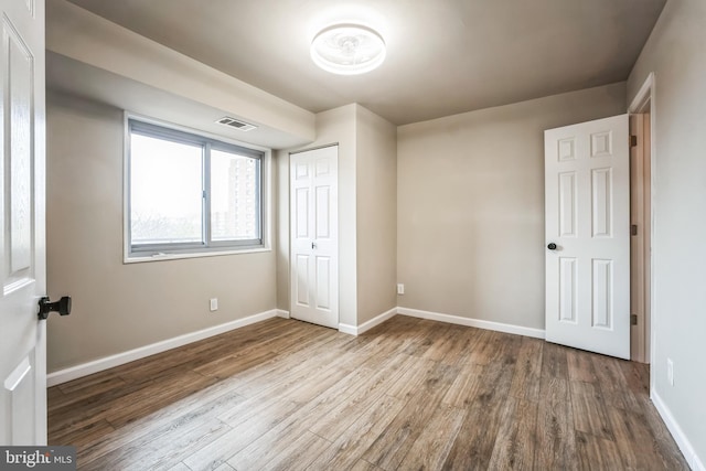 unfurnished bedroom featuring visible vents, baseboards, a closet, and wood finished floors