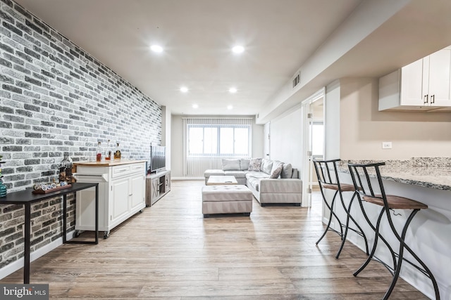 living room with recessed lighting, light wood-style flooring, brick wall, and visible vents