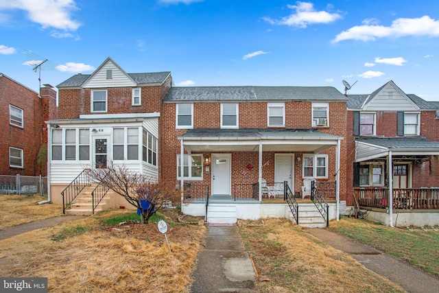 townhome / multi-family property featuring cooling unit, covered porch, brick siding, and fence