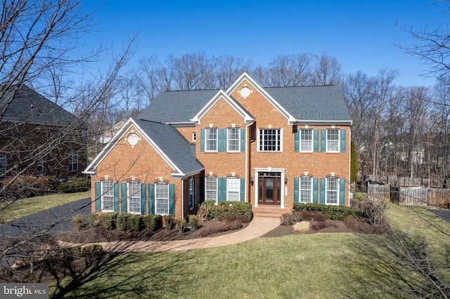 colonial-style house featuring a front yard, brick siding, and fence