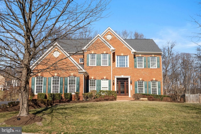 colonial inspired home with a front yard, fence, and brick siding