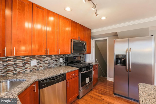 kitchen with wood finished floors, ornamental molding, appliances with stainless steel finishes, decorative backsplash, and brown cabinets