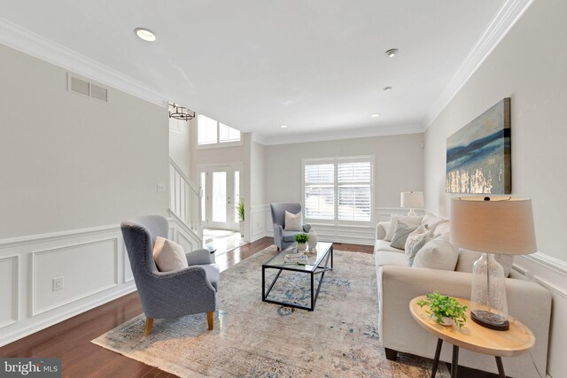 living area with wood finished floors, a wainscoted wall, visible vents, stairs, and crown molding