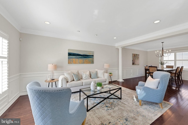 living area with a notable chandelier, ornamental molding, dark wood-style floors, a decorative wall, and ornate columns