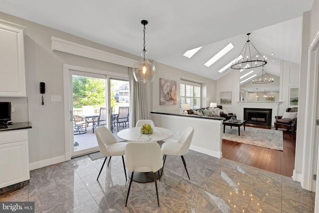 dining area featuring a notable chandelier, marble finish floor, vaulted ceiling with skylight, a fireplace, and baseboards