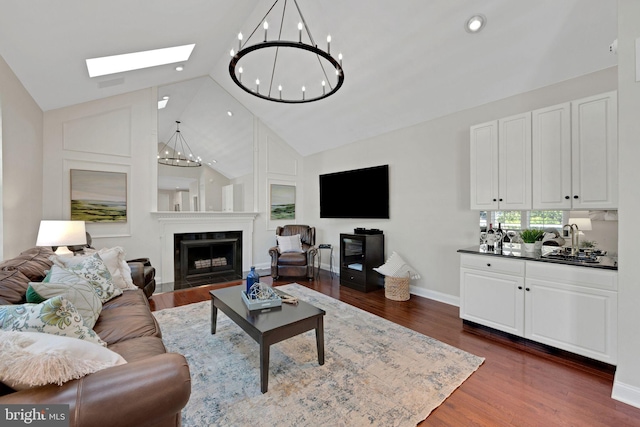 living room featuring dark wood-style floors, a fireplace with flush hearth, a skylight, and a notable chandelier