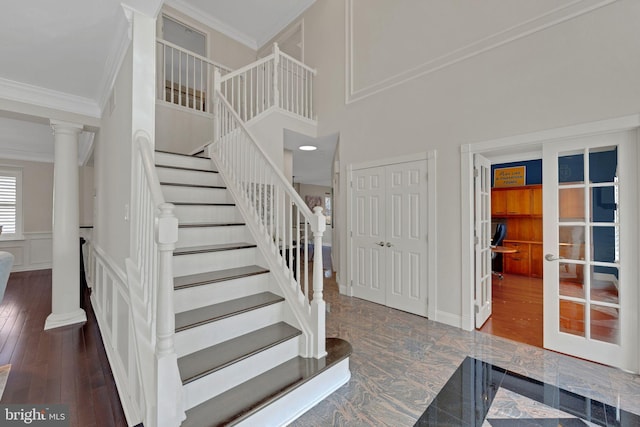 stairway with a wainscoted wall, ornamental molding, wood finished floors, a decorative wall, and decorative columns